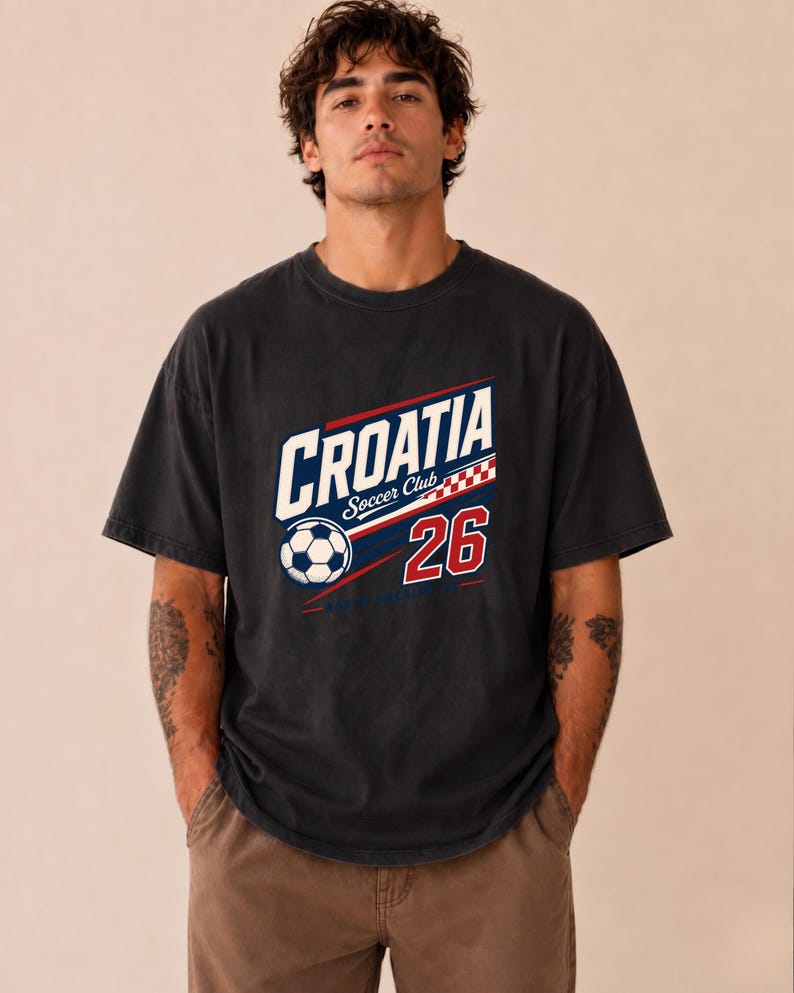 K&ouml;nnte beinhalten: Ein anthrazitfarbenes Kurzarm-T-Shirt mit einem Grafikdruck, der CROATIA Soccer Club mit einem Fu&szlig;ball-Symbol, einem rot-wei&szlig;en Karomuster und der Zahl 26 in Rot mit wei&szlig;er Umrandung auf der Vorderseite zeigt.