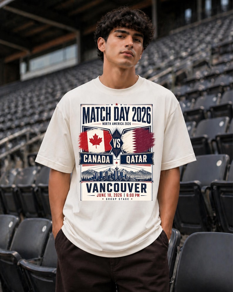 May include: A cream-colored t-shirt with a graphic promoting a soccer match. The design includes the text "MATCH DAY 2026" and "CANADA VS QATAR" with flags. The location and date are also displayed: "VANCOUVER JUNE 18, 2026 | 6:00 PM".