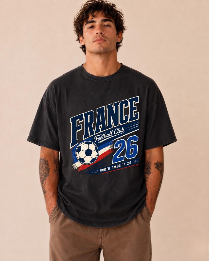 May include: A charcoal grey short-sleeve t-shirt featuring a graphic print with the text FRANCE, Football Club, and 26. The design includes a football, red, white, and blue brush strokes, and the text NORTH AMERICA 26 in a bold font.