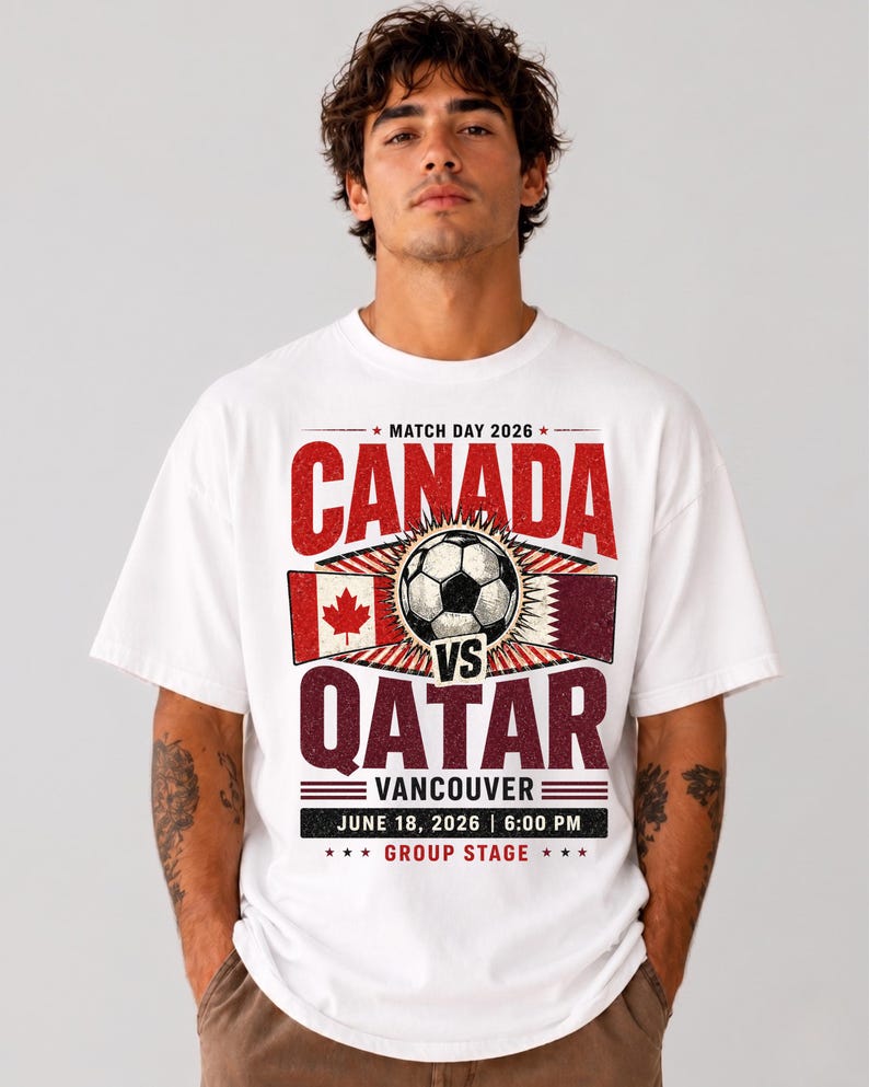 May include: White t-shirt featuring a soccer match graphic. The design includes the text "CANADA vs QATAR" with flags and a soccer ball. The text also includes "VANCOUVER", the date "JUNE 18, 2026", and "6:00 PM".