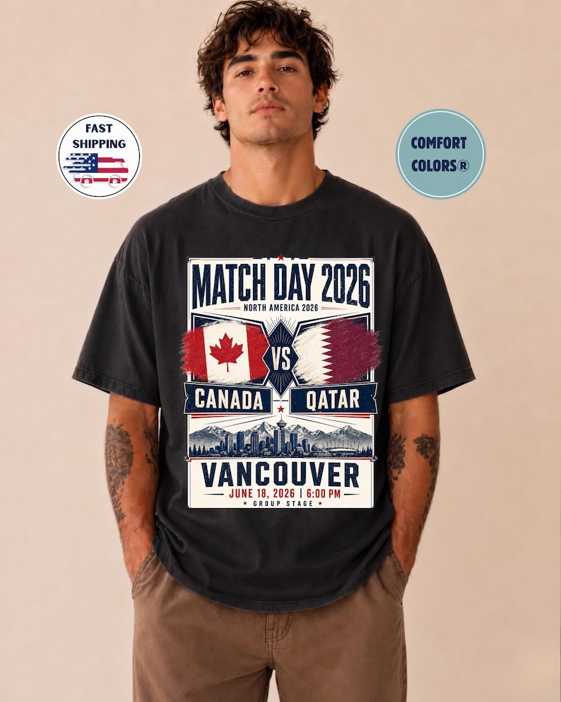 May include: Black t-shirt with a graphic for the 2026 Match Day between Canada and Qatar in Vancouver. The design includes the flags of Canada and Qatar, the date, and the time of the match.