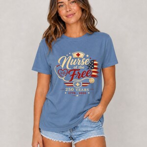 May include: A blue t-shirt with the text "Nurse of the Free" in gold script, featuring a red cross, a stethoscope, and an American flag design. The shirt also includes the text "250 YEARS 1776-2026".