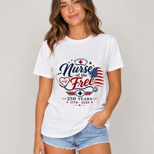 May include: White t-shirt with a graphic that reads "Nurse of the Free" in navy blue script, with a red heart and stethoscope design. The design also includes an American flag and the text "250 Years 1776-2026" in red and blue.