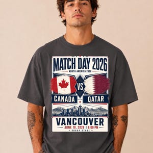 May include: Dark gray t-shirt featuring a graphic for the 2026 match between Canada and Qatar in Vancouver. The design includes the flags of both countries, the text "MATCH DAY 2026", and the date and time of the game.