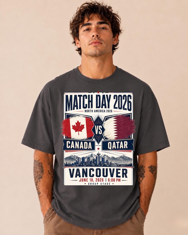 May include: Dark gray t-shirt featuring a graphic for the 2026 match between Canada and Qatar in Vancouver. The design includes the flags of both countries, the text "MATCH DAY 2026", and the date and time of the game.