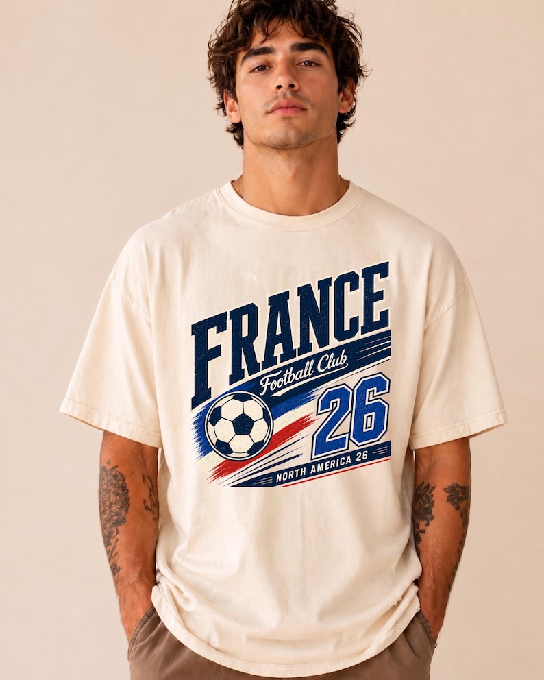 May include: An off-white short-sleeve t-shirt featuring a graphic print with the text FRANCE Football Club and the number 26. The design includes a football and red, white, and blue motion lines, with the text NORTH AMERICA 26 at the bottom.