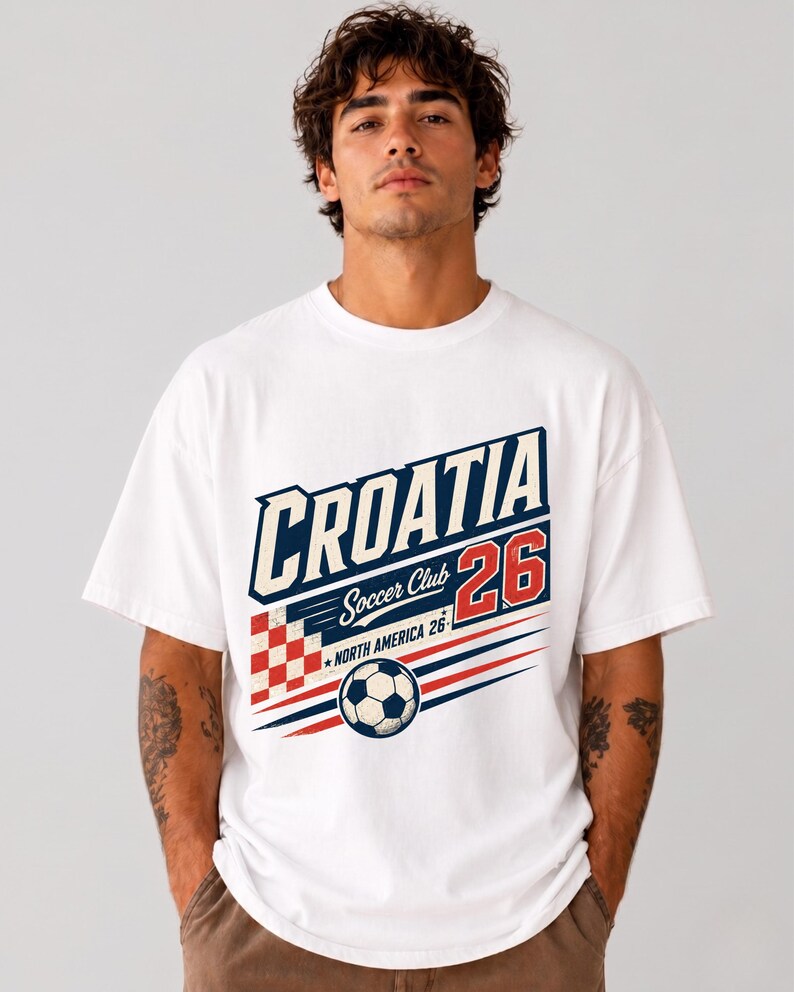 以下が含まれることがあります： CROATIA、Soccer Club、26、NORTH AMERICA 26というテキストがプリントされた白い半袖Tシャツ。デザインには、赤と白の市松模様の正方形、サッカーボール、赤と青の水平線が含まれています。