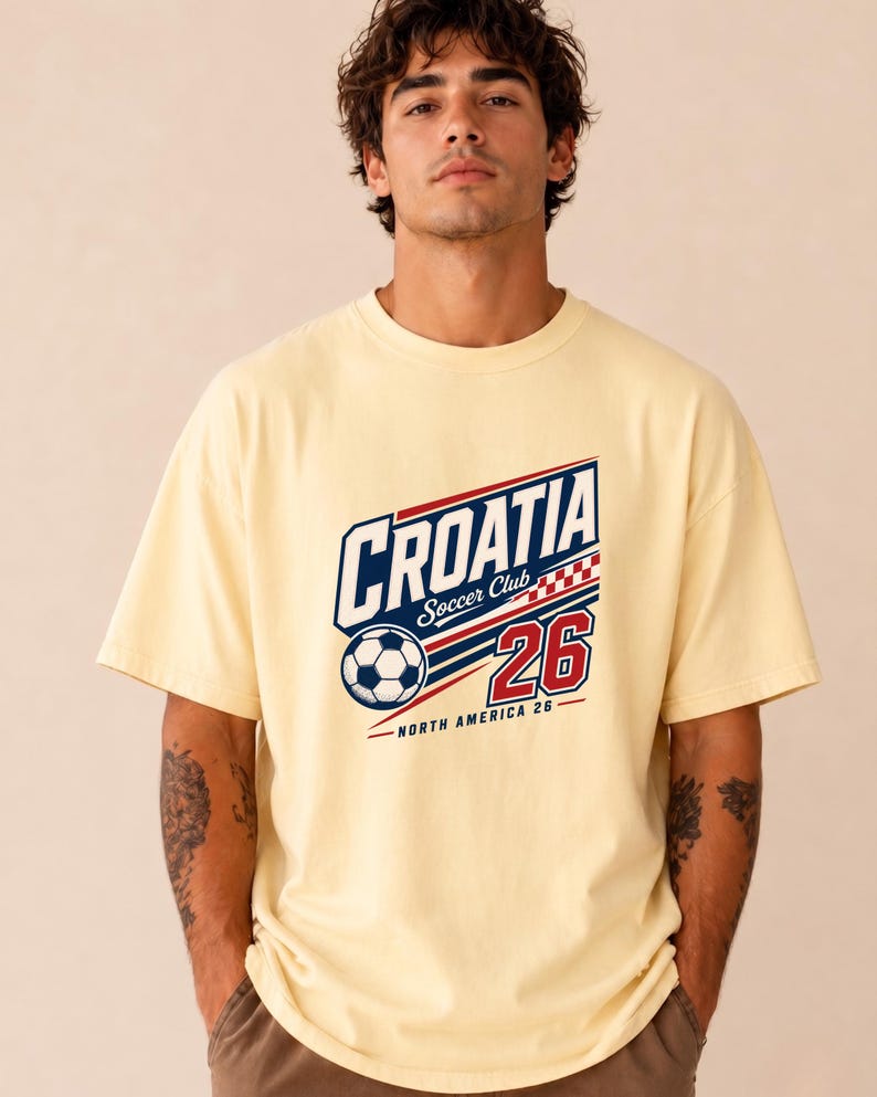 K&ouml;nnte beinhalten: Ein hellgelbes Kurzarm-T-Shirt mit einem Grafikdruck, der CROATIA Soccer Club 26 North America 26 zeigt. Das Design umfasst einen Fu&szlig;ball, ein rot-wei&szlig;es Karomuster sowie blauen und roten Text auf einem hellgelben Hintergrund.
