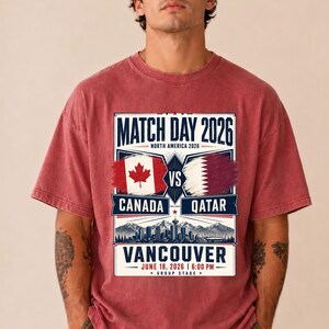 May include: Red t-shirt with a graphic promoting a soccer match. The design includes the text "MATCH DAY 2026" and "CANADA VS QATAR" with flags. The location is Vancouver, with the date June 18, 2026.
