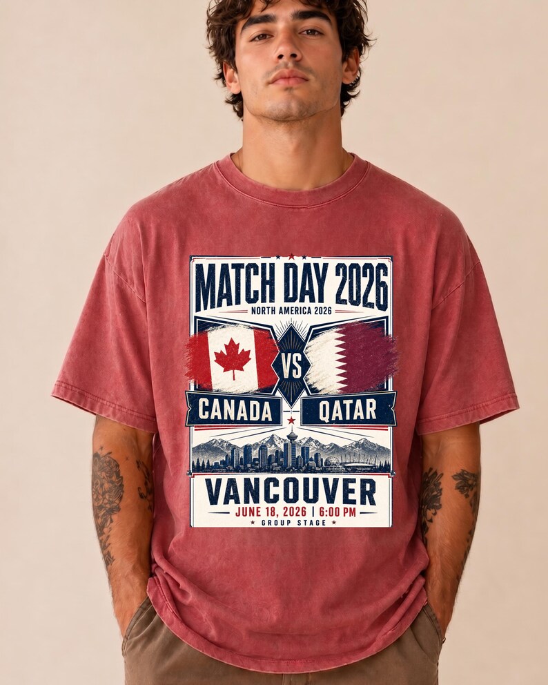 May include: Red t-shirt with a graphic promoting a soccer match. The design includes the text "MATCH DAY 2026" and "CANADA VS QATAR" with flags. The location is Vancouver, with the date June 18, 2026.