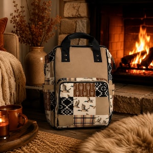 May include: A backpack featuring a solid tan top panel and a patchwork lower section. The patchwork design includes patterns of flying ducks, brown arrows, black and white geometric shapes, and a red, black, and white plaid pattern with black handles.
