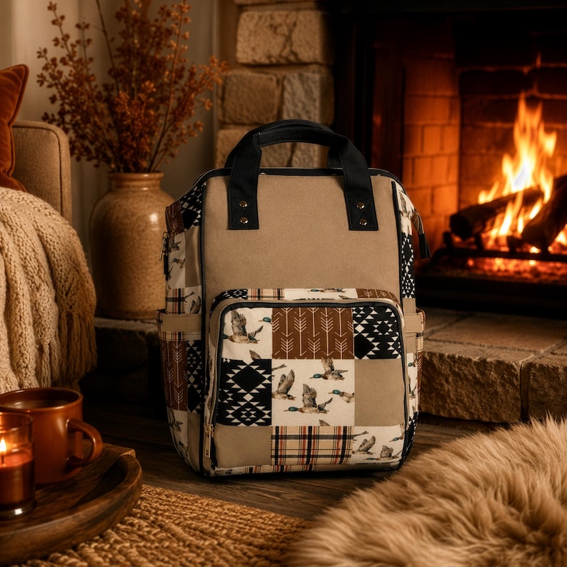 May include: A backpack featuring a solid tan top panel and a patchwork lower section. The patchwork design includes patterns of flying ducks, brown arrows, black and white geometric shapes, and a red, black, and white plaid pattern with black handles.