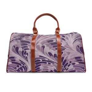 Può includere: Una borsa da viaggio con un motivo floreale viola e bianco. La borsa ha manici e cinghie in pelle marrone. La borsa misura circa 51 cm di lunghezza, 25 cm di larghezza e 25 cm di altezza.