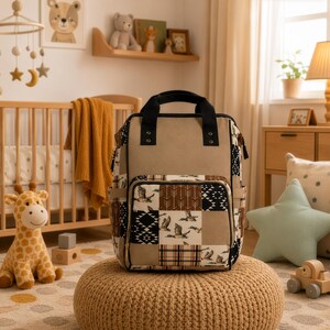 May include: A beige backpack featuring a patchwork design with patterns of flying ducks, brown arrows, black and white geometric shapes, and plaid. The bag has black top handles, a front zippered pocket, and side pockets with black trim accents.
