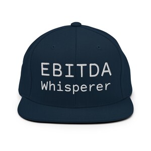 May include: A navy blue flat-brimmed baseball cap with the white text "EBITDA Whisperer" embroidered on the front. The cap has a structured crown and a flat brim, suitable for casual wear.