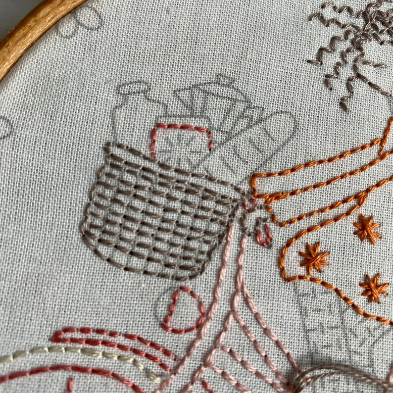 May include: Close-up of a brown and white embroidered basket filled with brown and white embroidered items. The basket is part of a larger embroidery design that includes a brown and orange embroidered figure.