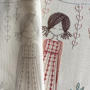 May include: Two embroidered figures of girls on a beige fabric. The girl on the left is outlined in grey thread and the girl on the right is embroidered in brown and red thread.
