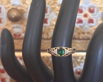 May include: A gold-toned ring with an emerald-cut green gemstone and small white accent stones. The ring has an open filigree design on the band. The ring is displayed on a black hand.