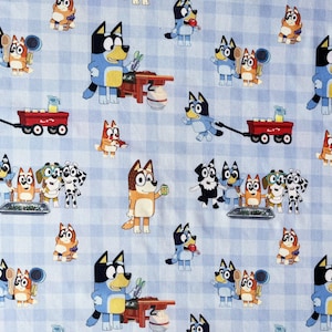 May include: A patterned fabric with cartoon dog characters on a light blue and white gingham background. The dogs are in various poses, some cooking, others pulling a red wagon. The design is repeated across the fabric.