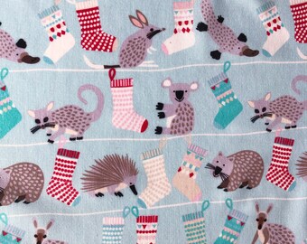 May include: A blue fabric with a repeating pattern of Australian animals and Christmas stockings. The animals include a kangaroo, echidna, wombat, koala, and possum. The stockings are in various colors and patterns.