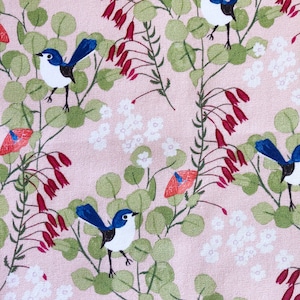 A close-up view of a premium pink cotton quilting fabric designed by Anne Waters. The fabric features a repeating pattern of small blue fairy wrens perched on delicate branches with green eucalyptus leaves and vibrant red Australian Christmas bell flowers.