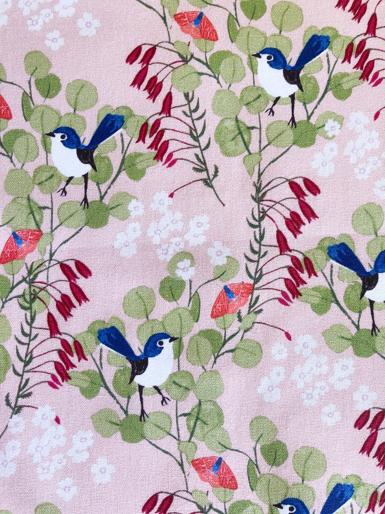 A close-up view of a premium pink cotton quilting fabric designed by Anne Waters. The fabric features a repeating pattern of small blue fairy wrens perched on delicate branches with green eucalyptus leaves and vibrant red Australian Christmas bell flowers.