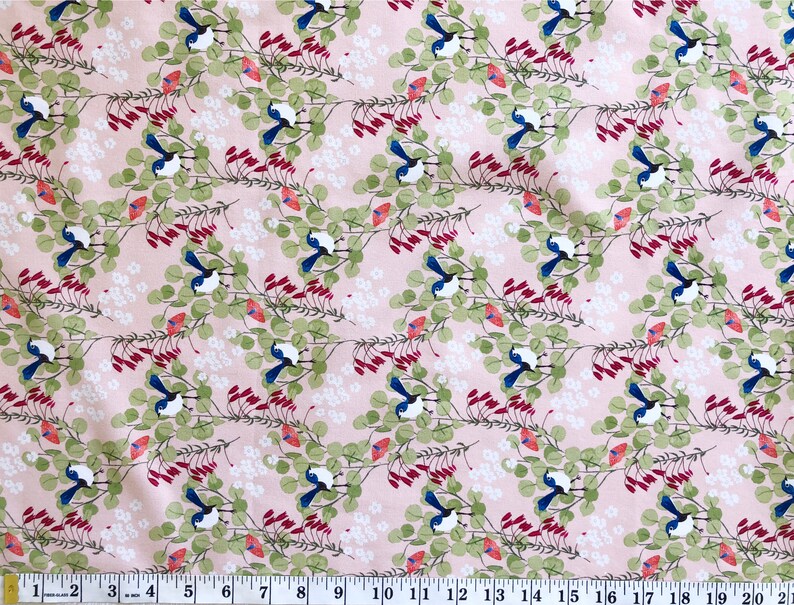 A close-up view of a premium pink cotton quilting fabric designed by Anne Waters. The fabric features a repeating pattern of small blue fairy wrens perched on delicate branches with green eucalyptus leaves and vibrant red Australian Christmas bell flowers.