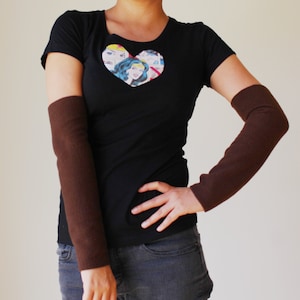 May include: A black t-shirt with a heart-shaped graphic featuring a comic book image of Wonder Woman. The shirt is paired with brown arm warmers.