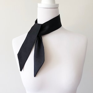 May include: A black neck scarf tied in a simple knot around a white mannequin's neck. The scarf is made of a smooth, silky fabric.