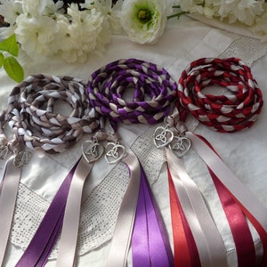 May include: Three braided satin ribbon cords in brown, purple, and red color combinations. Each cord features a silver-toned metal heart-shaped charm with a triquetra knot design, finished with long, loose satin ribbon tails in matching colors.