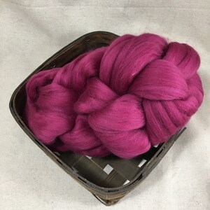 Puede incluir: Una gran cantidad de fibra de lana rosa oscuro en una cesta tejida. La lana es suave y esponjosa, y es perfecta para hilar o fieltro.