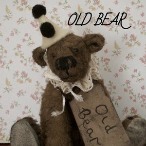 May include: A brown teddy bear wearing a white and black jester hat. The bear is holding a sign that says "Old Bear".