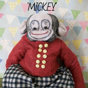 May include: A handmade plush monkey toy with a black and white checkered pattern pants, a red jacket with yellow buttons, and a black face with a painted smile. The toy is labeled 'Mickey'.