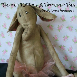 May include: A handmade rag doll elephant wearing a pink tutu and pink ballet shoes. The doll has a sad expression and is holding pink ribbons in its feet. The doll is sitting on a floral patterned background. The text "Tangled Ribbons & Tattered Toes" and "Mama's Little Moonbeam" is written above the doll.