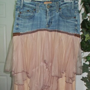 May include: A denim skirt with a layered, ruffled tulle overlay. The tulle is a light pink color and the denim is a medium blue.