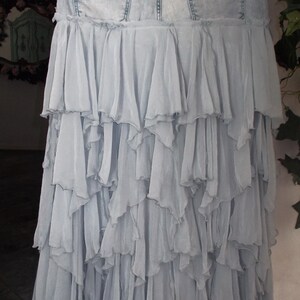 May include: A light blue denim skirt with a layered, ruffled chiffon design. The skirt features a denim waistband with back pockets and a cascading, tiered chiffon skirt. The skirt is hanging on a hanger.