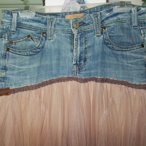 May include: A denim skirt with a brown lace trim and a tulle overlay. The skirt is a light blue color and has a brown belt.