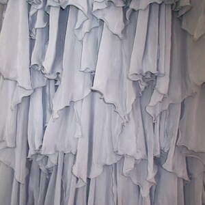 May include: Close-up of a light blue fabric with multiple layers of ruffled edges. The fabric appears to be lightweight and flowing, with a soft, textured appearance. The ruffles create a cascading effect.