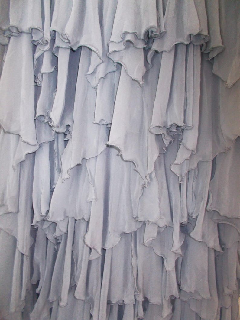 May include: Close-up of a light blue fabric with multiple layers of ruffled edges. The fabric appears to be lightweight and flowing, with a soft, textured appearance. The ruffles create a cascading effect.