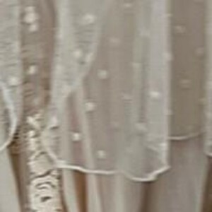 May include: A layered, off-white dress with delicate lace and sheer, dotted fabric. The dress features intricate details and a flowing design, suggesting a bohemian or vintage style. The image highlights the dress's texture and construction.