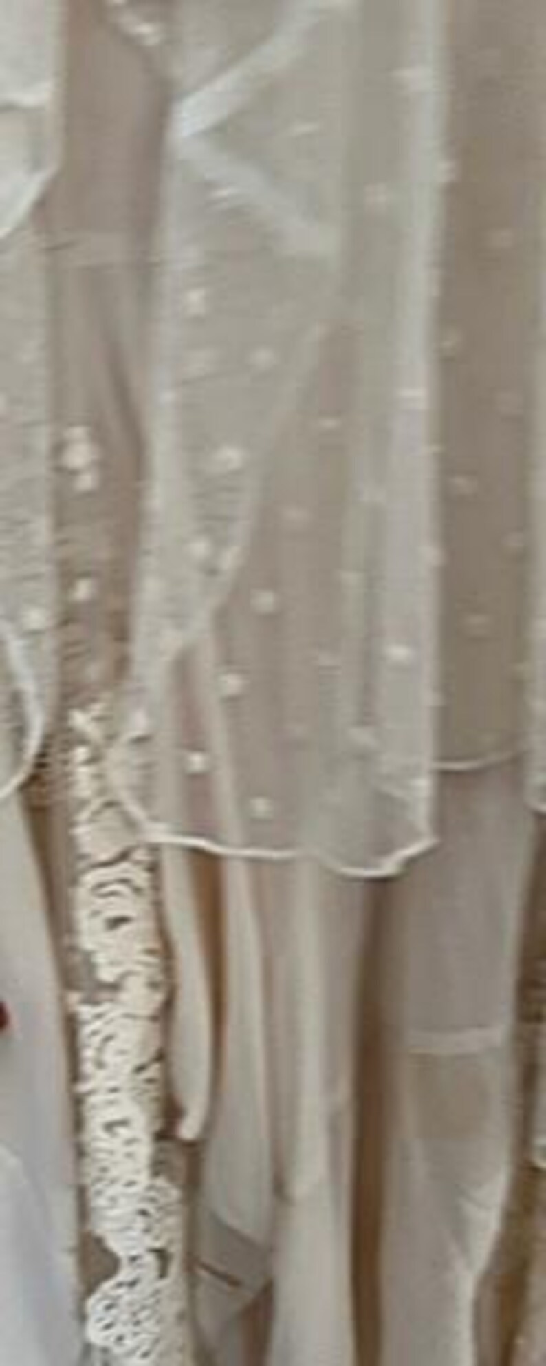 May include: A layered, off-white dress with delicate lace and sheer, dotted fabric. The dress features intricate details and a flowing design, suggesting a bohemian or vintage style. The image highlights the dress's texture and construction.