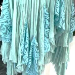 Puede incluir: Una falda fluida con volantes en tonos azul claro y aguamarina. La falda presenta m&uacute;ltiples capas de tela con aplicaciones de encaje en un azul contrastante. El dise&ntilde;o crea un efecto bohemio y en capas, adecuado para ropa casual.