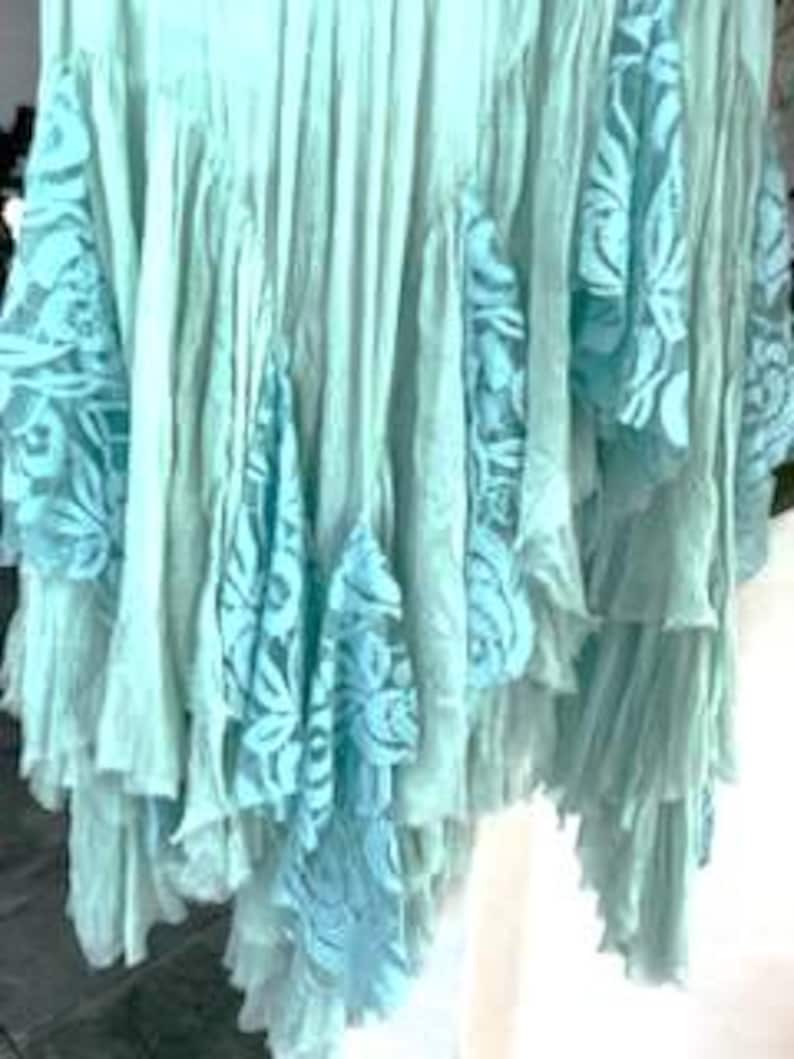 Puede incluir: Una falda fluida con volantes en tonos azul claro y aguamarina. La falda presenta m&uacute;ltiples capas de tela con aplicaciones de encaje en un azul contrastante. El dise&ntilde;o crea un efecto bohemio y en capas, adecuado para ropa casual.