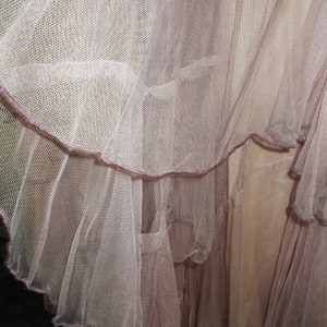 May include: A close-up of a pale pink tulle skirt with multiple layers. The skirt has a ruffled hem and a delicate, sheer texture.