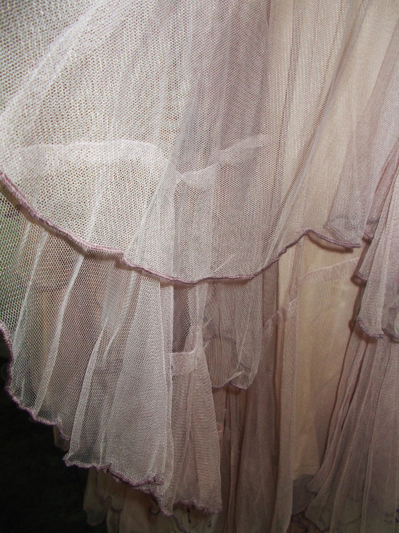 May include: A close-up of a pale pink tulle skirt with multiple layers. The skirt has a ruffled hem and a delicate, sheer texture.