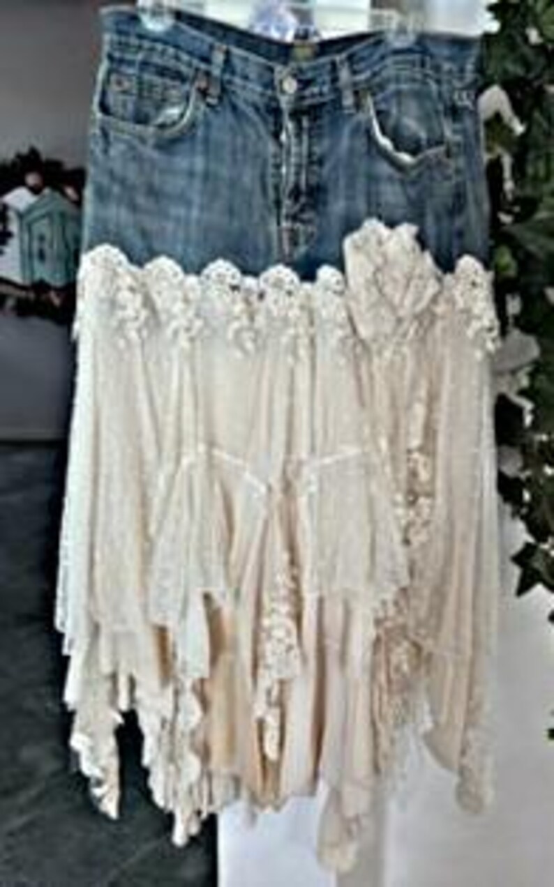 May include: A denim skirt with a layered, off-white lace and fabric design. The skirt features a classic blue jean waistband and pockets, transitioning into a cascading, bohemian-style lace skirt. The lace has intricate floral patterns.