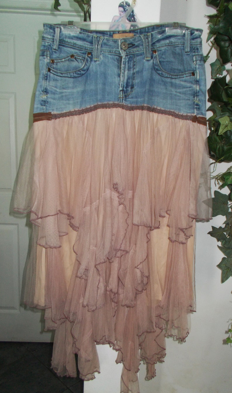 May include: A denim skirt with a layered, ruffled tulle overlay. The tulle is a light pink color and the denim is a medium blue.