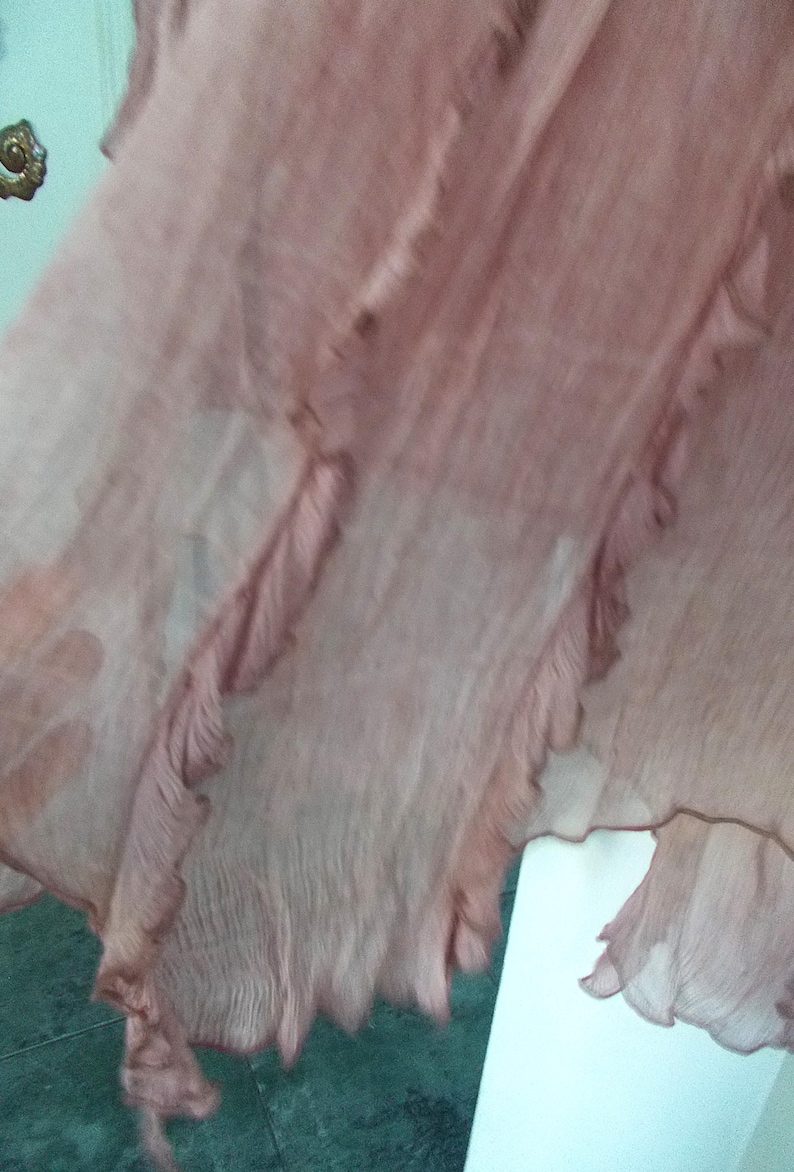Op de afbeelding: Een vloeiende, transparante stof in tinten van stoffig roze. De stof heeft een gelaagd ontwerp met gerimpelde randen, waardoor een delicate en luchtige uitstraling ontstaat. Het materiaal lijkt lichtgewicht en mogelijk zijde of een vergelijkbare vezel.