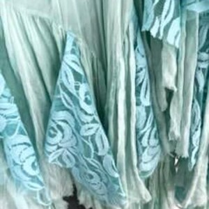 Puede incluir: Primer plano de una tela verde claro con capas de volantes y detalles de encaje. El encaje presenta un delicado dise&ntilde;o floral en un tono azul claro a juego. La tela parece suave y fluida.