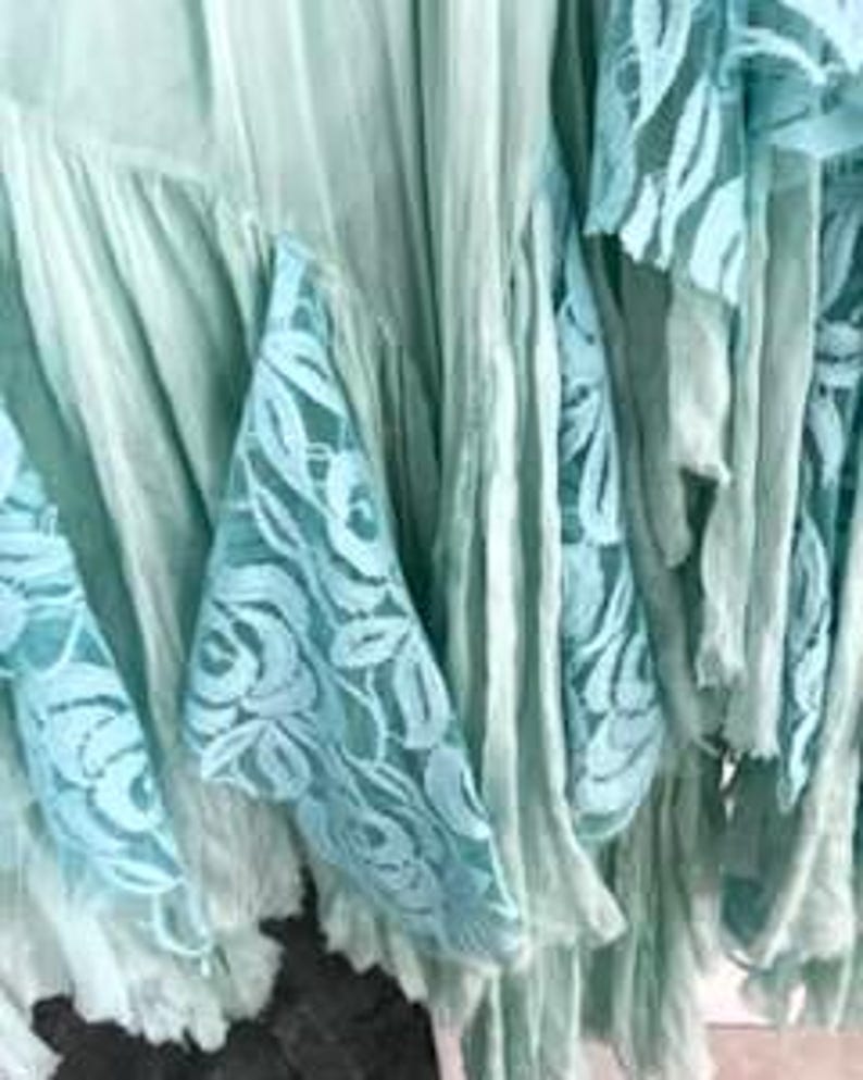 Puede incluir: Primer plano de una tela verde claro con capas de volantes y detalles de encaje. El encaje presenta un delicado dise&ntilde;o floral en un tono azul claro a juego. La tela parece suave y fluida.